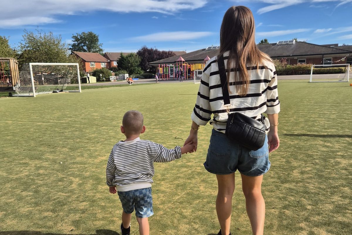 A mum and toddler walking hand in hand across a playing field